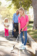 Mother And Daughters Picking Up Litter In Suburban Street