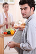 young woman cooking and boyfriend reading newspaper