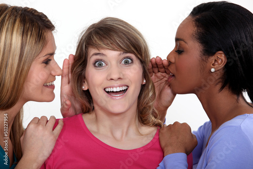 Photo: Two women whispering into friends ear Two women whispering into friends ear