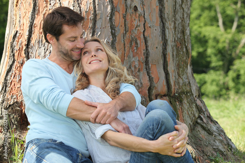 Photo: Happy couple sat by tree Happy couple sat by tree