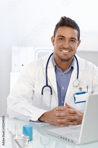 Photo: Happy doctor sitting at desk Happy doctor sitting at desk