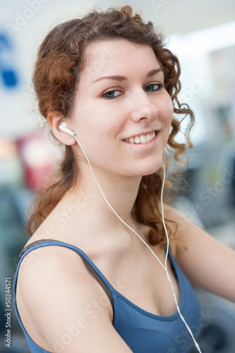 Photo: Young woman portrait in the gym while listening to music. Young woman portrait in the gym while listening to music.