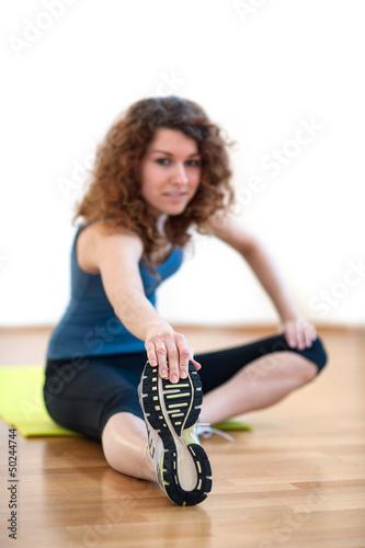 Photo: Young woman stretching her leg in the gym. Young woman stretching her leg in the gym.