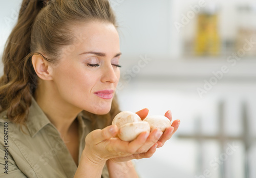Photo: Young housewife smelling mushroom in kitchen Young housewife smelling mushroom in kitchen