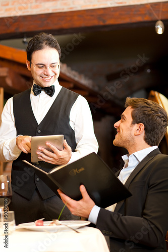 Photo: Young man at the restaurant ordering meal to a waiter Young man at the restaurant ordering meal to a waiter