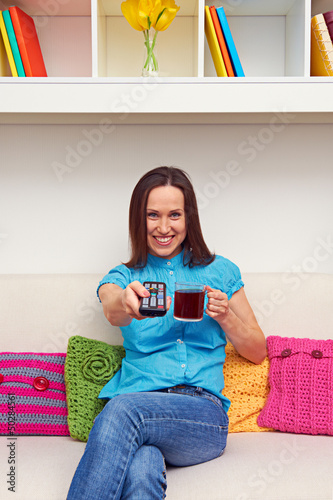 Photo: woman holding cup of tea and remote controller woman holding cup of tea and remote controller