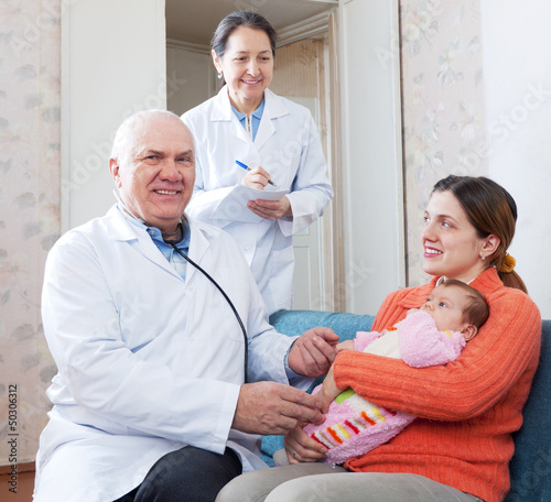 Photo: doctors examining baby in arms of happy woman doctors examining baby in arms of happy woman