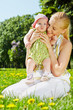 Young smiling mother sits on grass in park and holds her baby