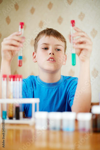 Photo: Boy in blue t-shirt sits at table with chemical reagents Boy in blue t-shirt sits at table with chemical reagents