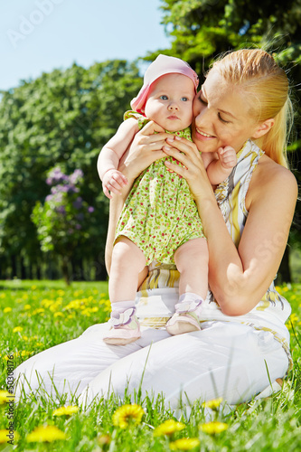 Photo: Young smiling mother sits on grass in park and holds her baby Young smiling mother sits on grass in park and holds her baby