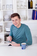 Photo: young man sitting with a tablet pc and tea cup in the kitchen young man sitting with a tablet pc and tea cup in the kitchen