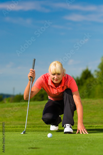 Photo: Young female golf player on course aiming for put Young female golf player on course aiming for put