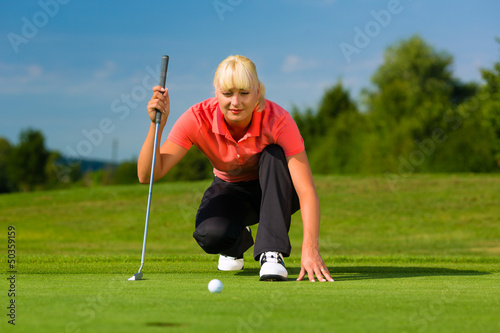 Photo: Young female golf player on course aiming for put Young female golf player on course aiming for put
