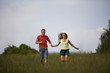 A young couple running through a field hand in hand