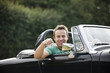 A young man sitting in a black sports car holding the keys
