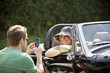 A young man photographing a young woman in a black sports car