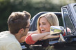 A young man speaking to a young woman in a black sports car