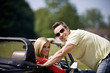 A young man standing next to a young woman in a black sports car