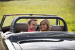 A young couple in a black sports car smiling