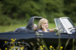 A young woman driving a black sports car holding a mobile phone