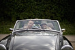 A young couple in a sports car with gardening tools in the back