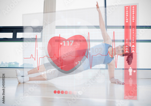 Photo: Woman doing yoga while looking at futuristic interface showing h Woman doing yoga while looking at futuristic interface showing h