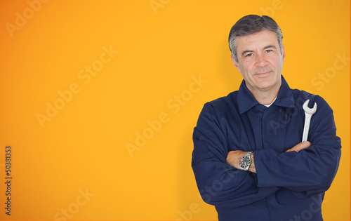 Photo: Mature mechanic standing in front of yellow background Mature mechanic standing in front of yellow background