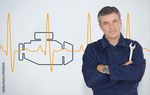 Photo: Mature mechanic standing in front of an engine background Mature mechanic standing in front of an engine background