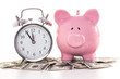 Pink piggy bank beside alarm clock on dollars