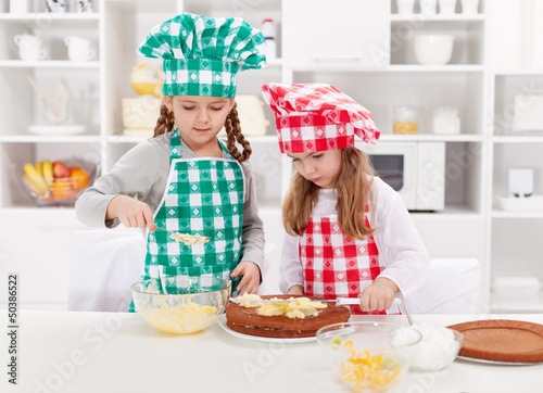 Photo: Little girls with chef hats preparing a cake Little girls with chef hats preparing a cake