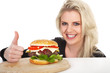 Hübsche junge Frau mit Hamburger lacht Daumen hoch