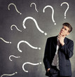 Businessman thinking, question marks on a wall