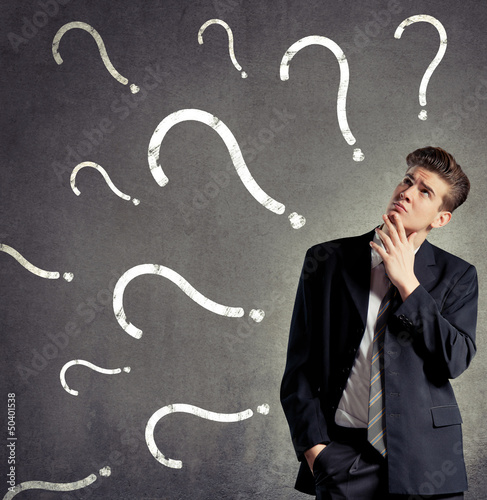 Photo: Businessman thinking, question marks on a wall Businessman thinking, question marks on a wall