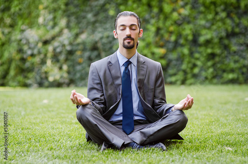 Photo: Young businessman meditating in the garden Young businessman meditating in the garden