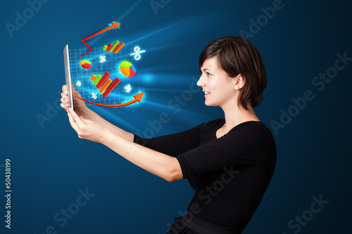 Photo: Young woman looking at modern tablet with abstract lights and va Young woman looking at modern tablet with abstract lights and va