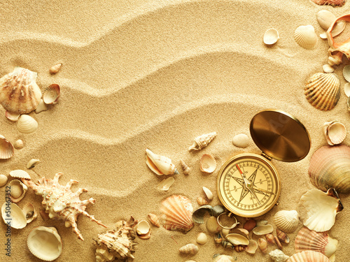 Photo: sea shells with sand as background and old compass sea shells with sand as background and old compass