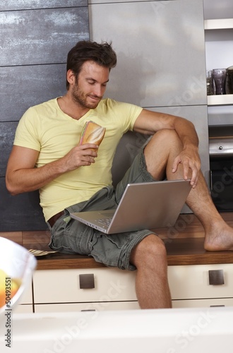 Photo: Young man with laptop in kitchen Young man with laptop in kitchen