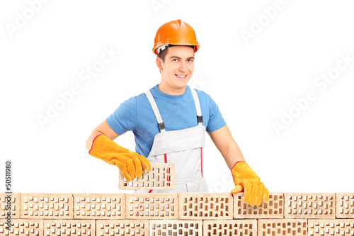 Photo: Male construction worker holding a brick behind brick wall Male construction worker holding a brick behind brick wall