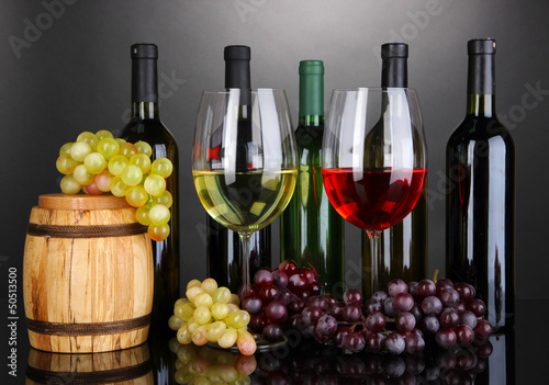 Photo: Assortment of wine in glasses and bottles on grey background Assortment of wine in glasses and bottles on grey background