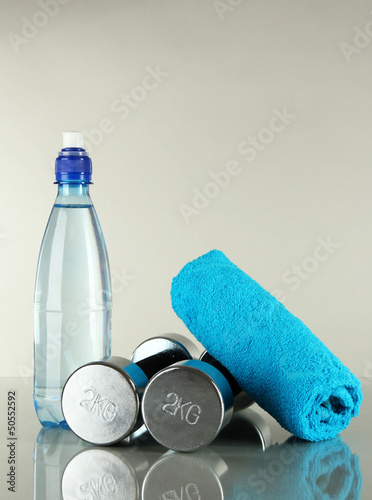 Photo: Dumbbells with towel and bottle of water on grey background Dumbbells with towel and bottle of water on grey background