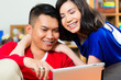 Indonesian couple sitting with tablet computer on couch