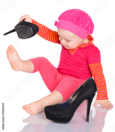 Photo: Cute little baby girl trying on her mother's shoes on white back Cute little baby girl trying on her mother's shoes on white back