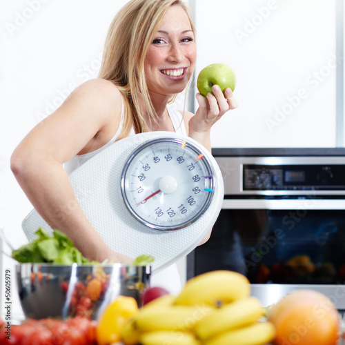 Photo: Girl with scale and fruits in kitchen is proud to lose weight Girl with scale and fruits in kitchen is proud to lose weight