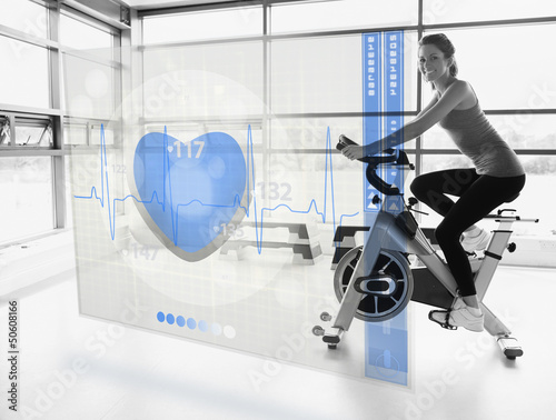 Photo: Young attractive girl doing exercise bike with futuristic interf Young attractive girl doing exercise bike with futuristic interf