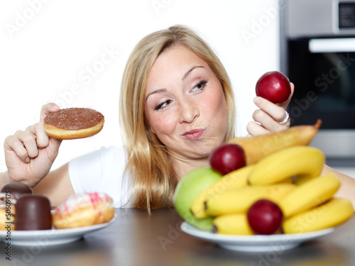 Photo: Pretty woman dithers between fruits or sweets Pretty woman dithers between fruits or sweets