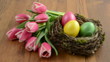 Easter eggs in bird nest with bunch of pink tulips