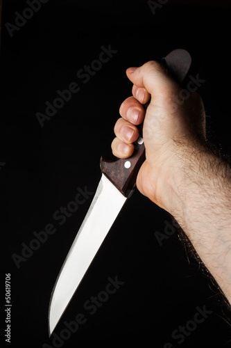 Photo: Hairy male hand holding a knife over a black background Hairy male hand holding a knife over a black background