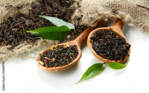 Photo: Dry tea with green leaves in wooden spoons, isolated on white Dry tea with green leaves in wooden spoons, isolated on white