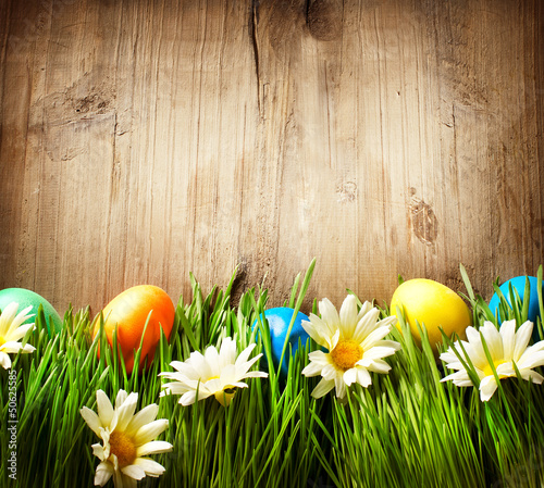 Photo: Colorful Easter Eggs in Spring Grass and Flowers over Wood Colorful Easter Eggs in Spring Grass and Flowers over Wood