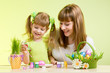 mother and child girl paint easter eggs over green background